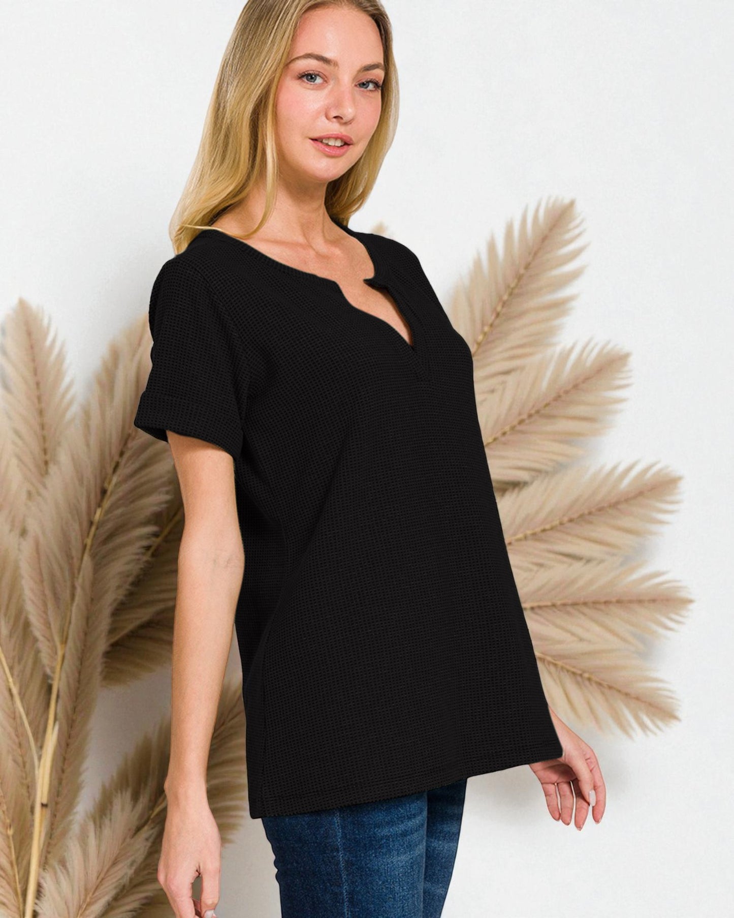 Woman wearing a black top with a white background and decorative plants.