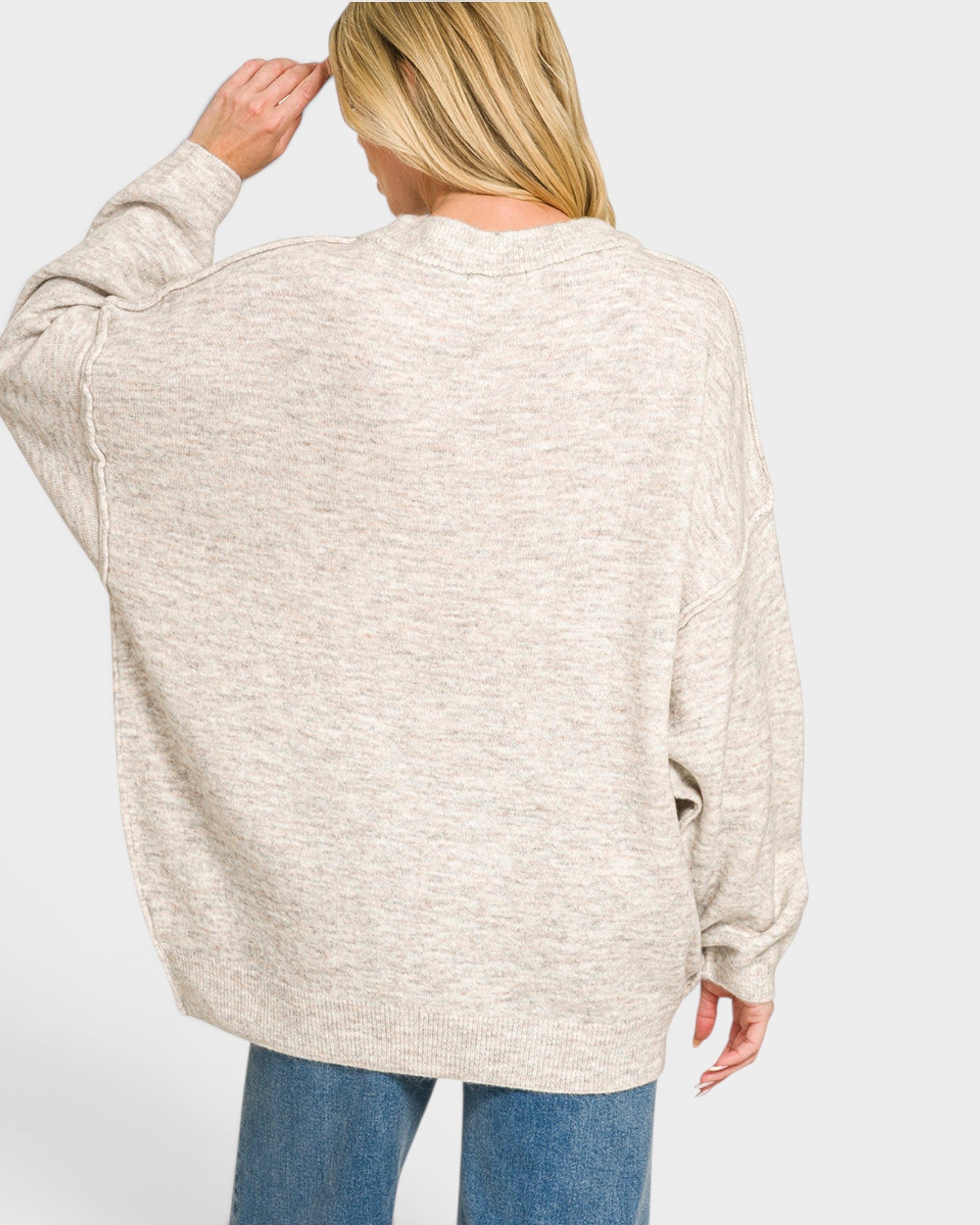 Person wearing a beige sweater and blue jeans on a white background