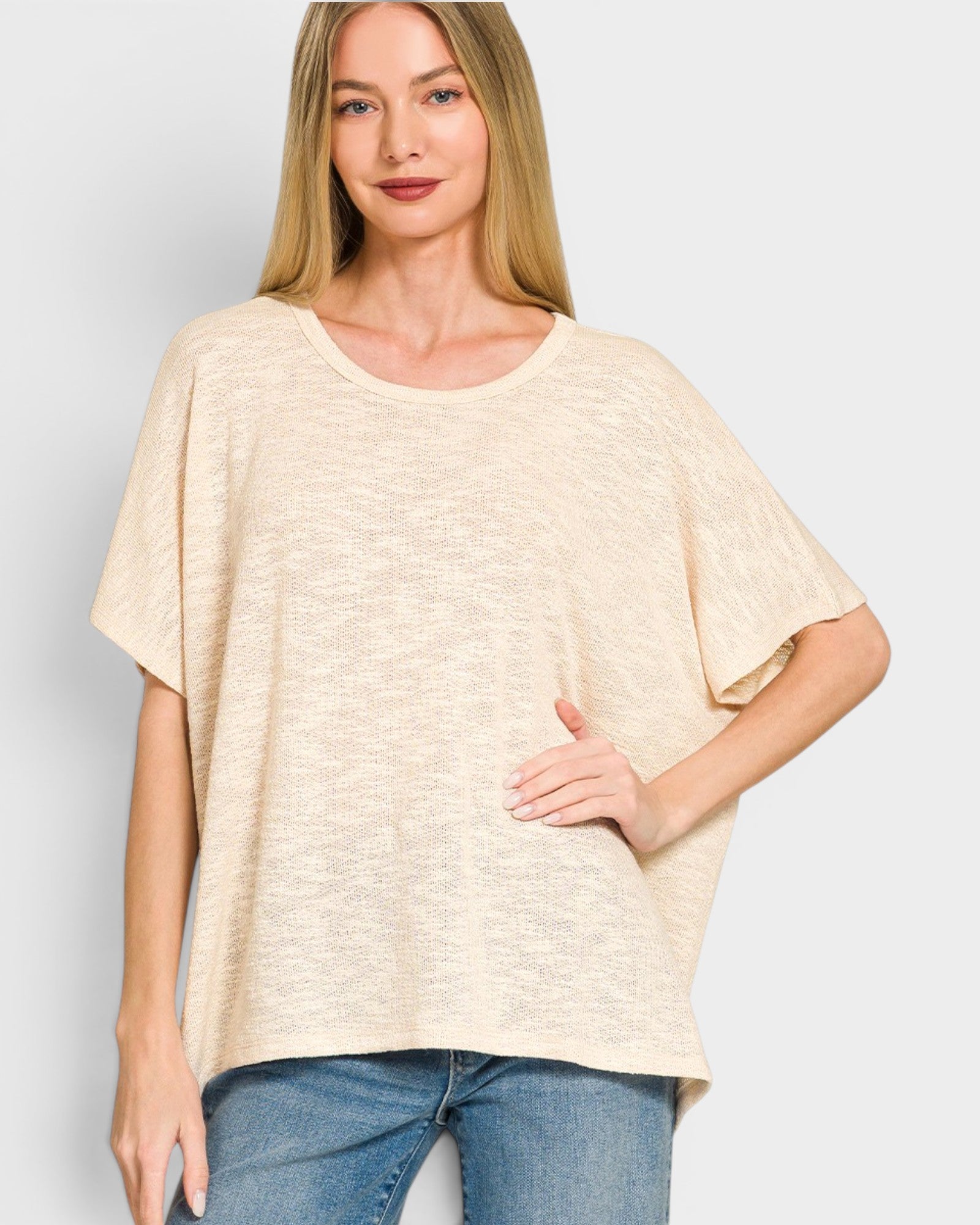 Woman wearing a beige oversized shirt and blue jeans on a light gray background