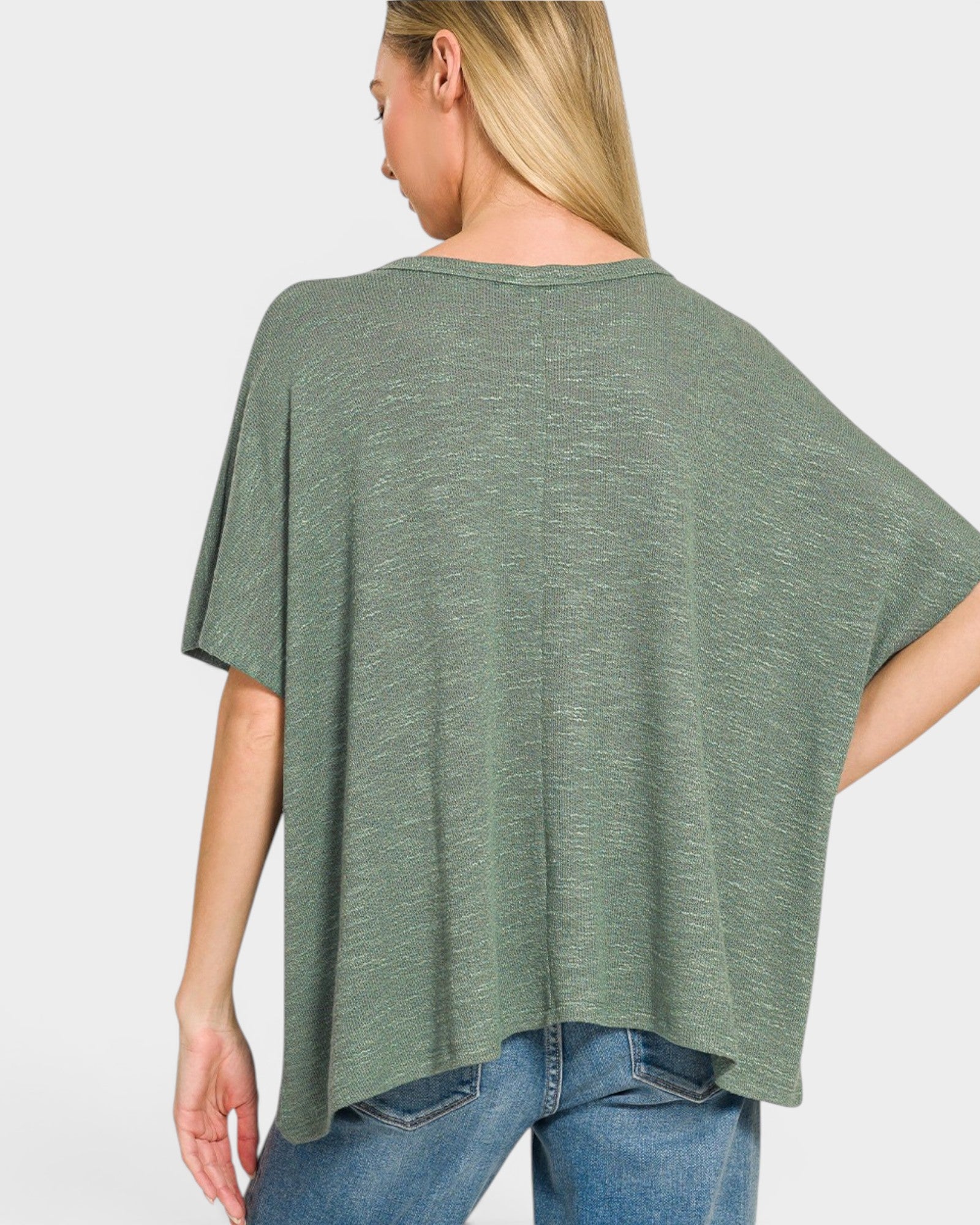 Woman wearing a green oversized t-shirt and blue jeans on a light gray background
