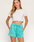 Woman wearing a white crop top and teal shorts on a plain background