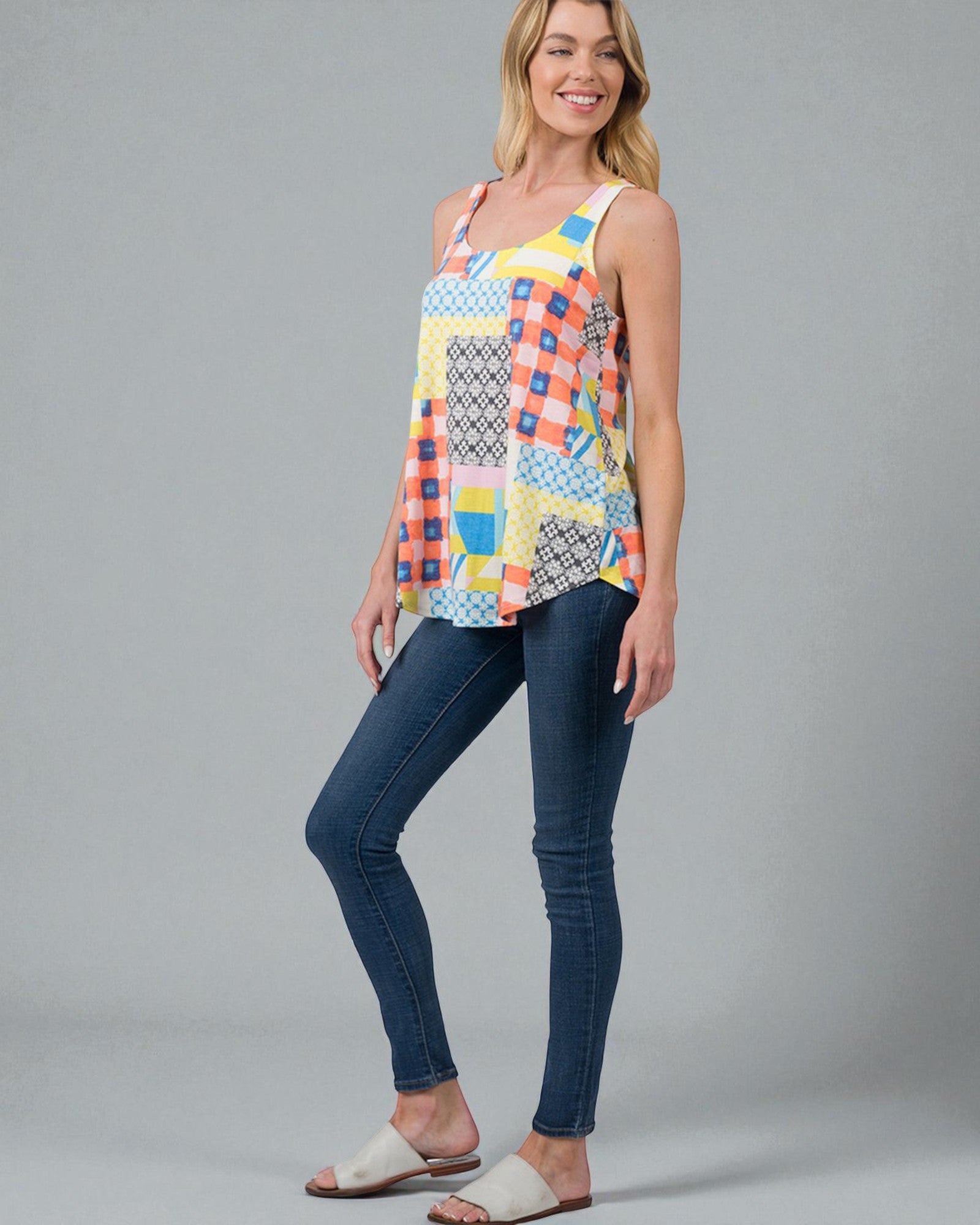 Woman wearing a colorful patterned top and blue jeans on a gray background