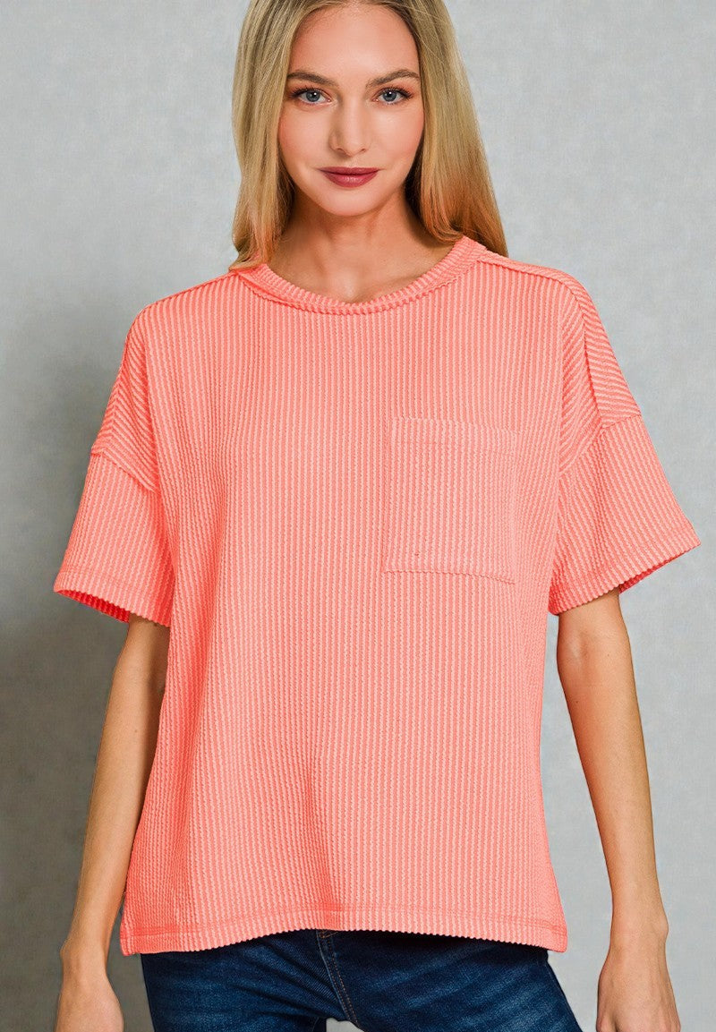 Woman wearing a coral ribbed top against a gray background