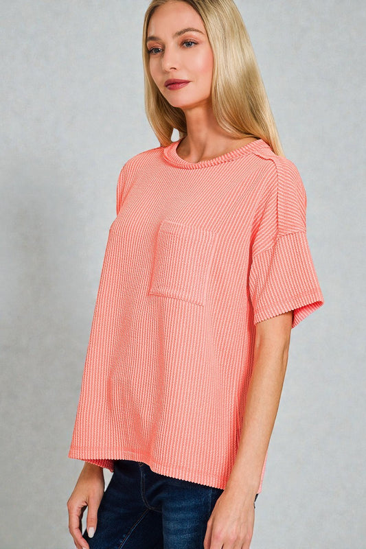 Woman wearing a coral ribbed top against a gray background