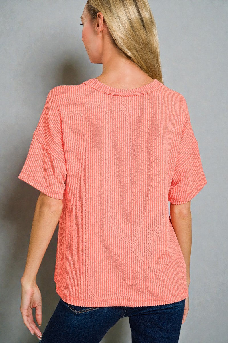 Woman wearing a coral ribbed top against a gray background
