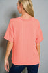 Woman wearing a coral ribbed top against a gray background