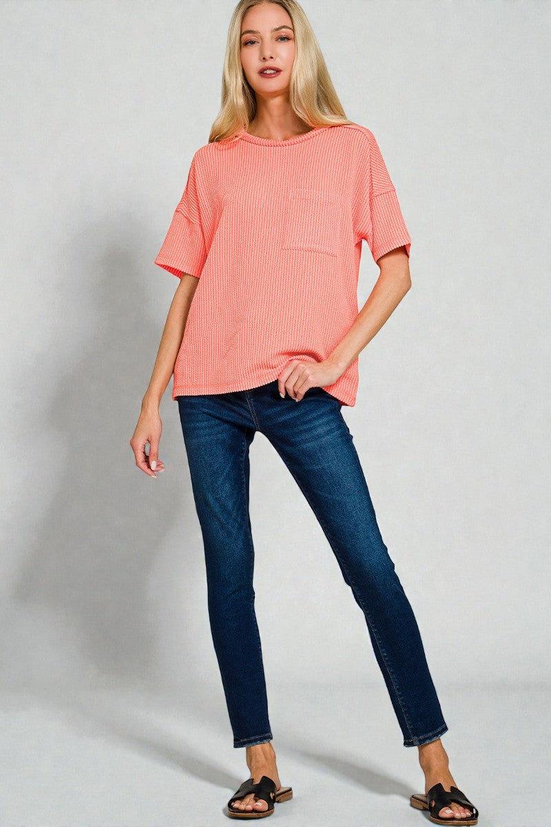 Woman wearing a coral top and blue jeans on a plain background