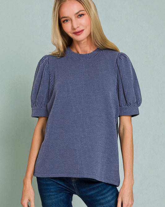 Woman wearing a blue striped blouse with puff sleeves against a gray background