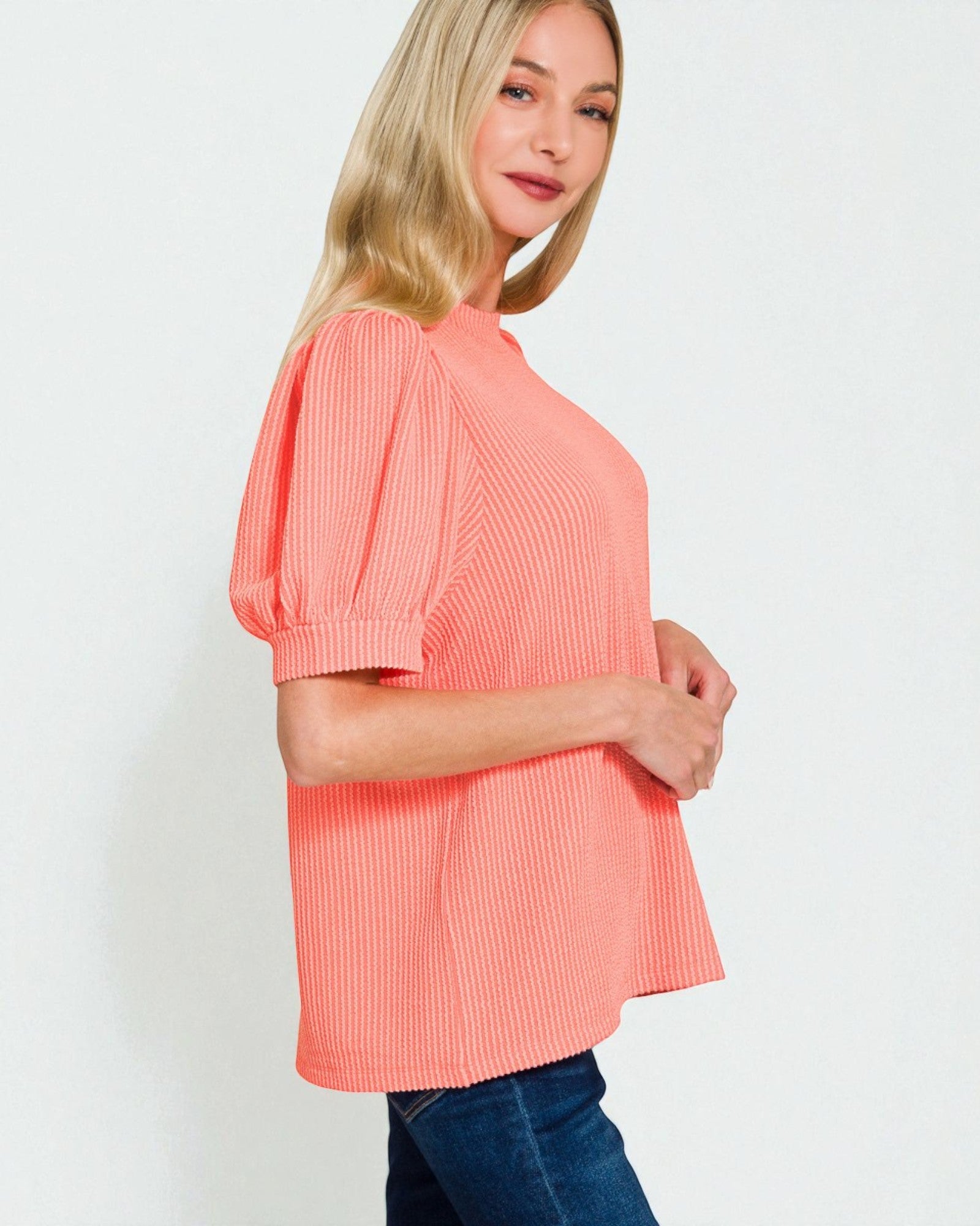 Woman wearing a coral ribbed top against a white background