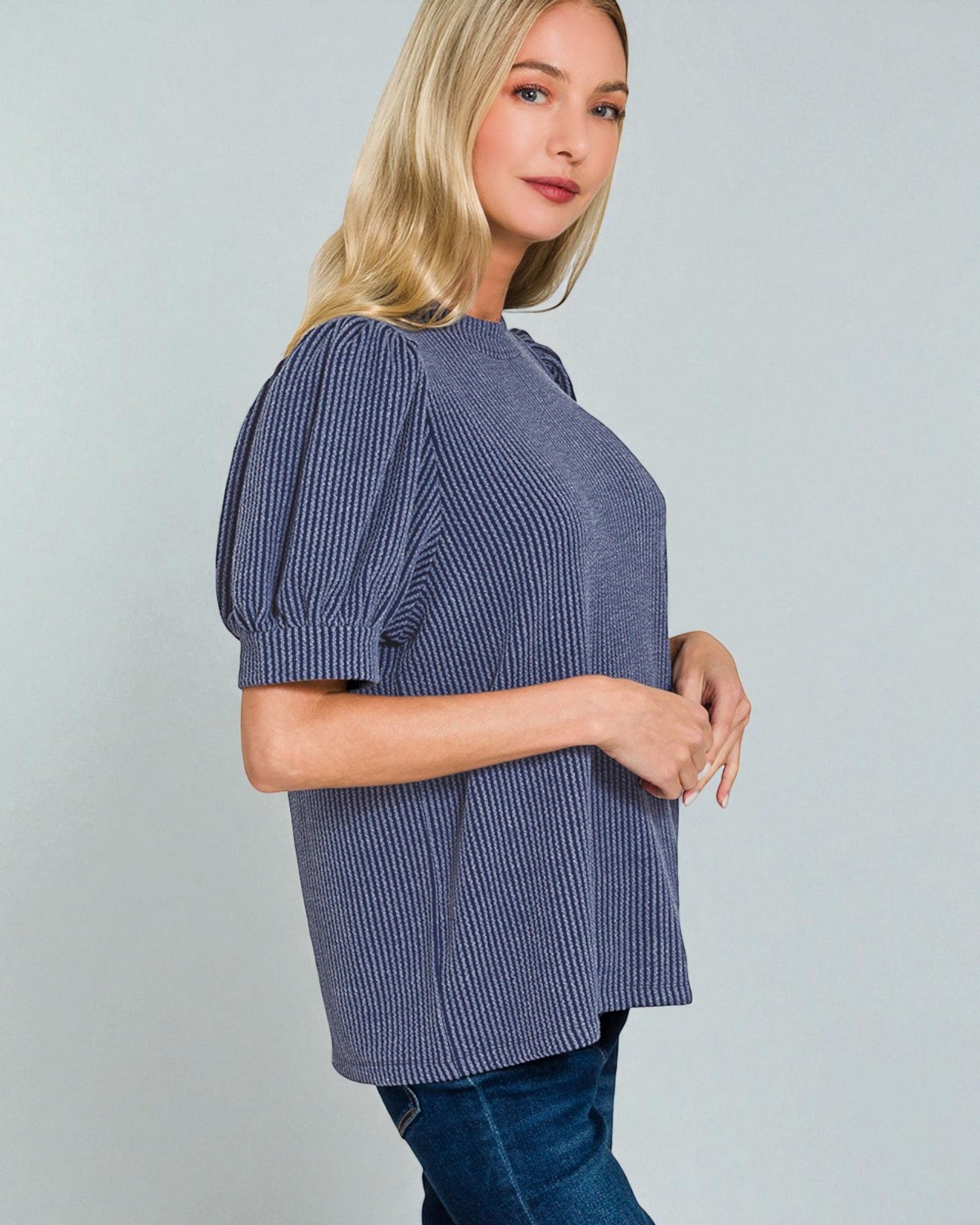 Woman wearing a blue ribbed sweater against a gray background