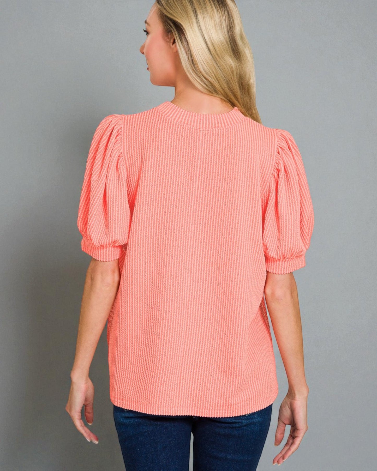 Woman wearing a coral blouse with puff sleeves against a gray background