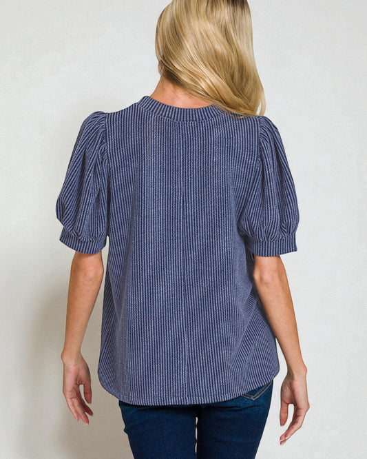 Woman wearing a blue striped blouse with puffed sleeves on a plain background