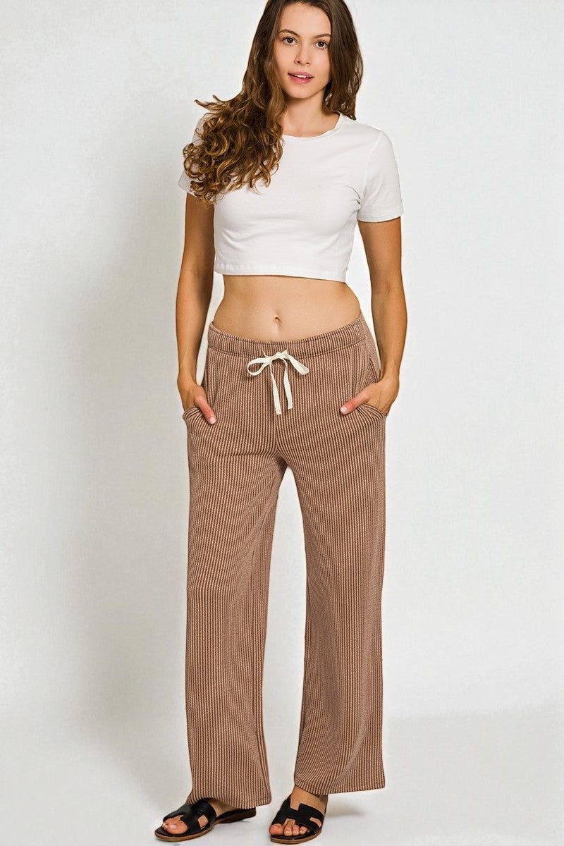 Woman wearing a white crop top and brown ribbed pants on a plain background