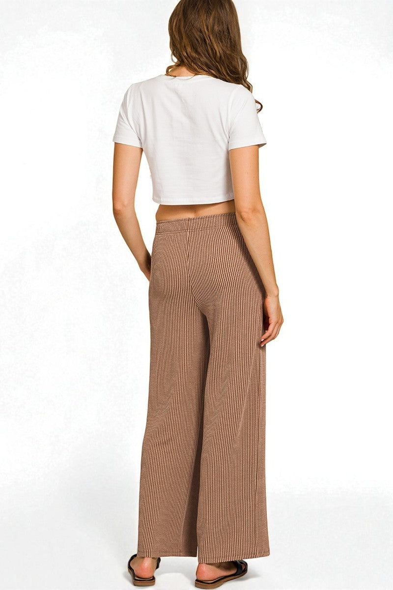 Woman wearing a white crop top and brown ribbed wide-leg pants on a white background