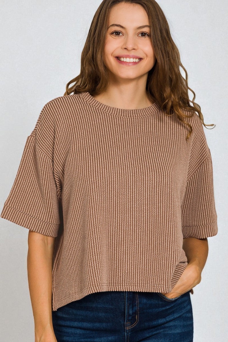 Woman wearing a brown ribbed sweater against a plain background