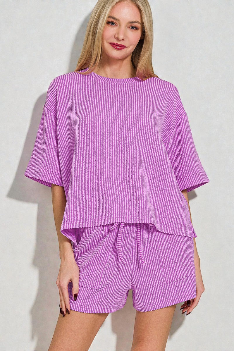 Woman wearing a purple ribbed top and shorts set against a white background