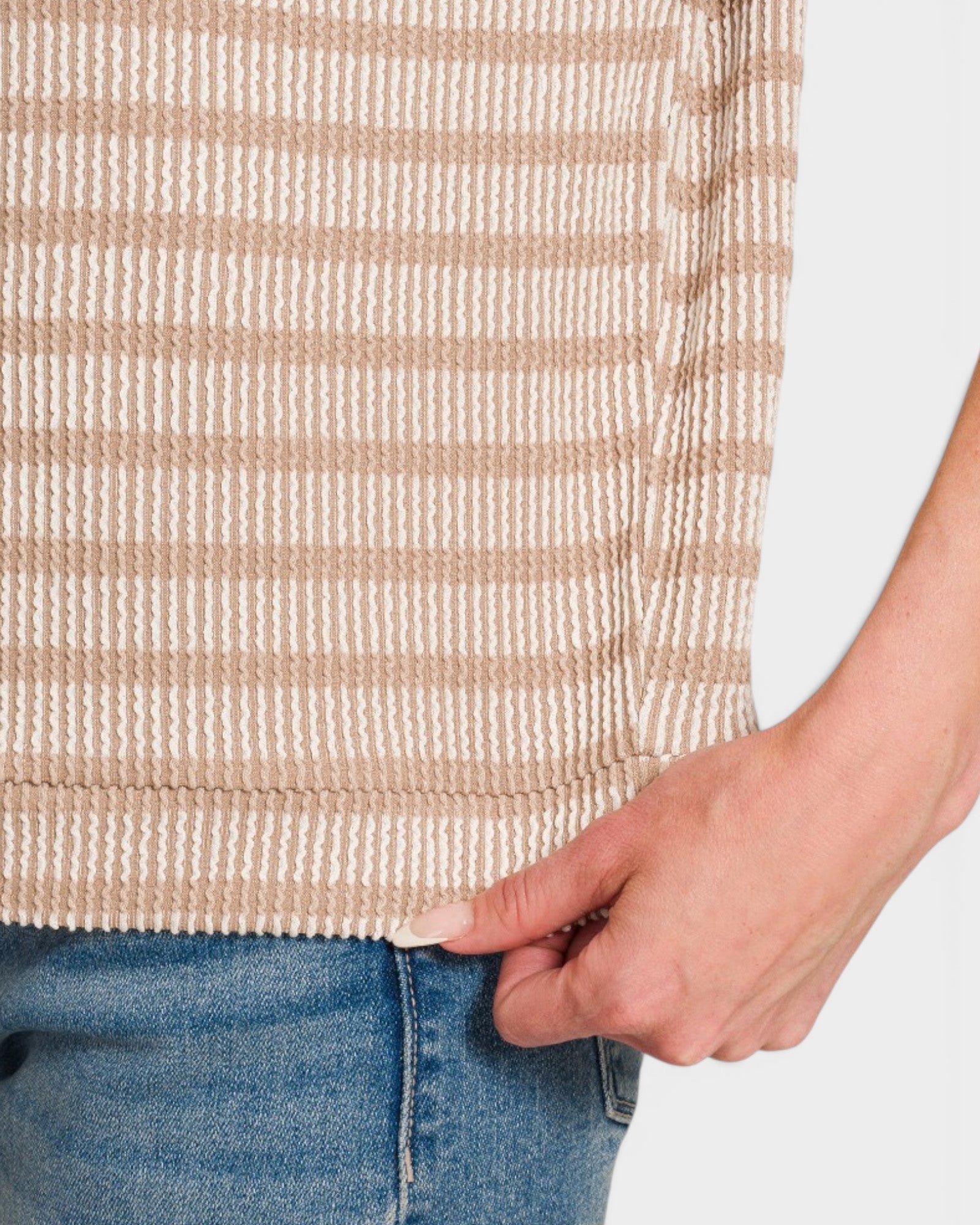 Close-up of a person wearing a beige and white striped sweater with blue jeans.