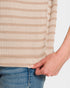 Close-up of a person wearing a beige and white striped sweater with blue jeans.