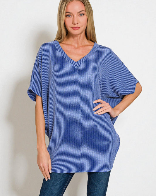 Woman wearing a blue ribbed oversized sweater against a plain background