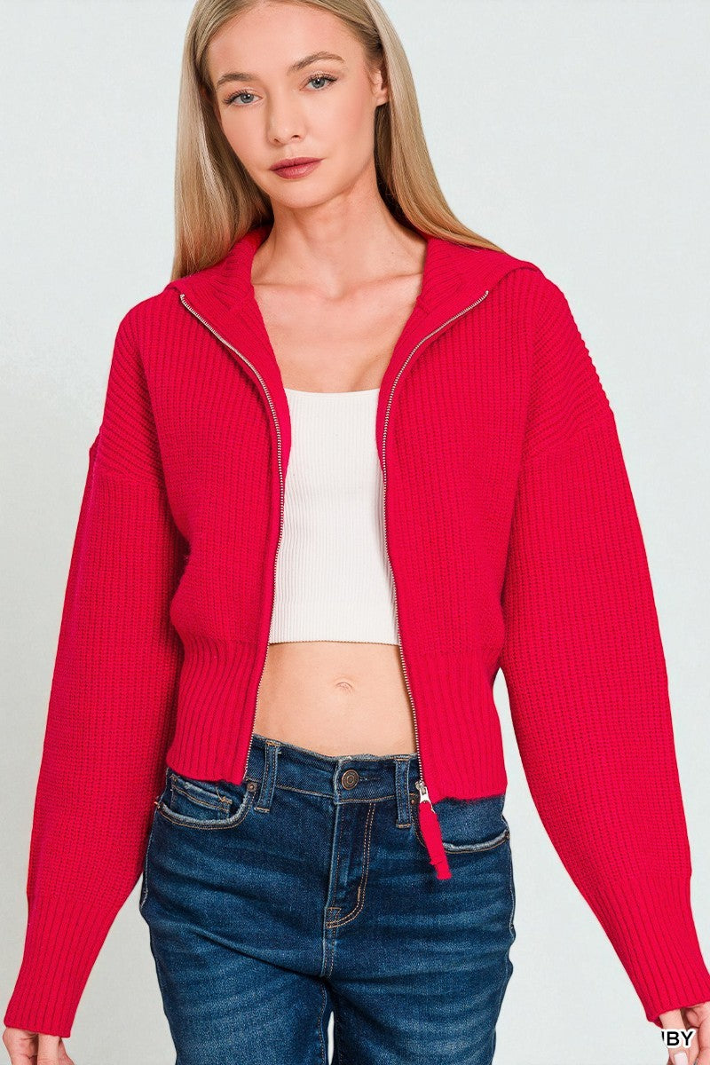 Woman wearing a red cropped cardigan over a white top and blue jeans on a light gray background