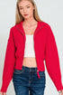 Woman wearing a red cropped cardigan over a white top and blue jeans on a light gray background