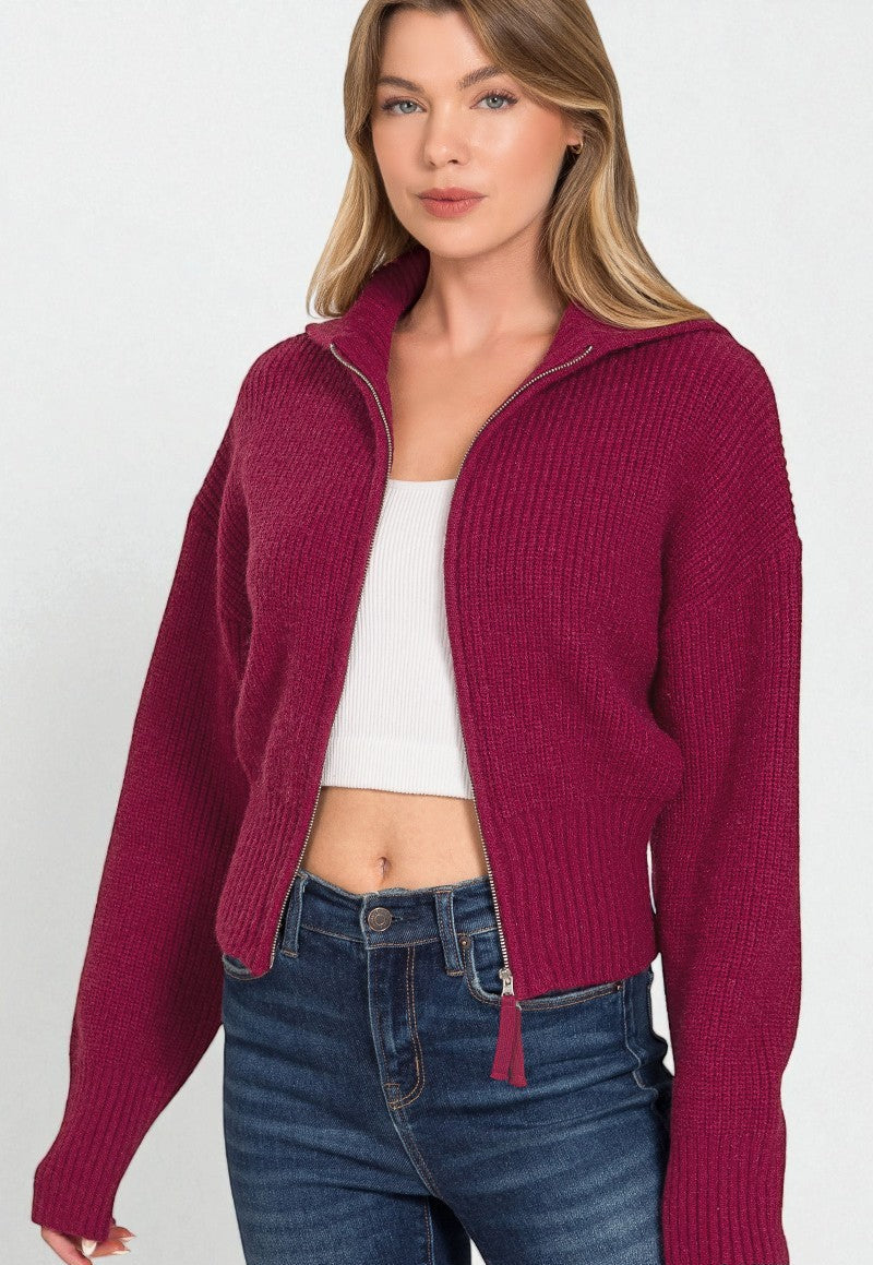 Woman wearing a burgundy zip-up sweater over a white top and blue jeans on a white background