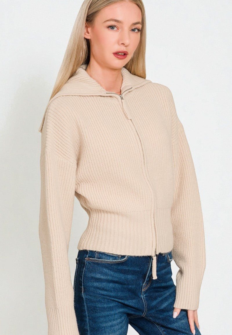 Woman wearing a beige ribbed sweater and blue jeans on a white background