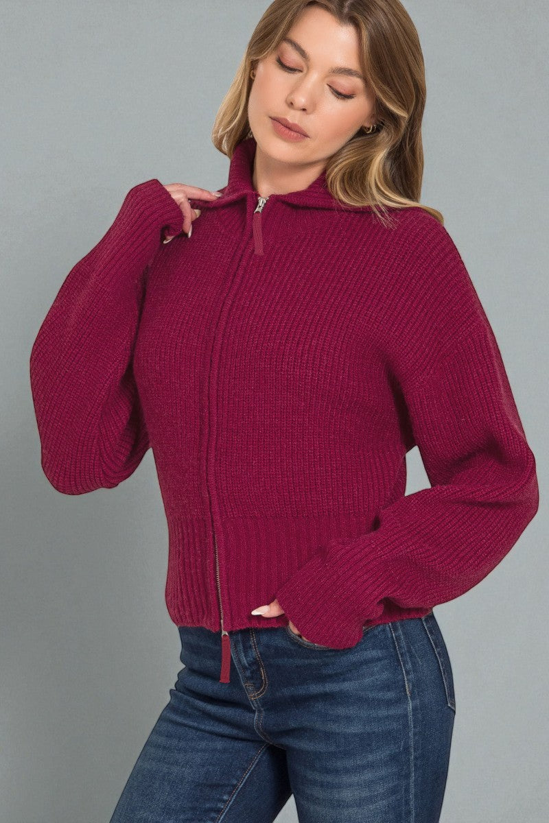 Woman wearing a maroon zip-up sweater against a gray background