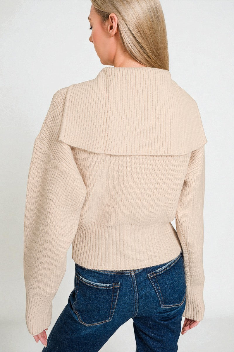 Woman wearing a beige ribbed sweater and blue jeans on a white background