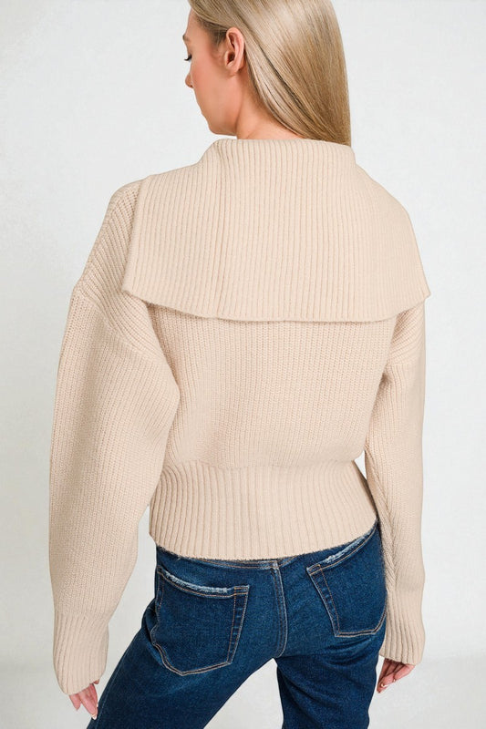 Woman wearing a beige ribbed sweater and blue jeans on a white background