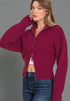Woman wearing a magenta zip-up sweater over a white top and blue jeans on a gray background