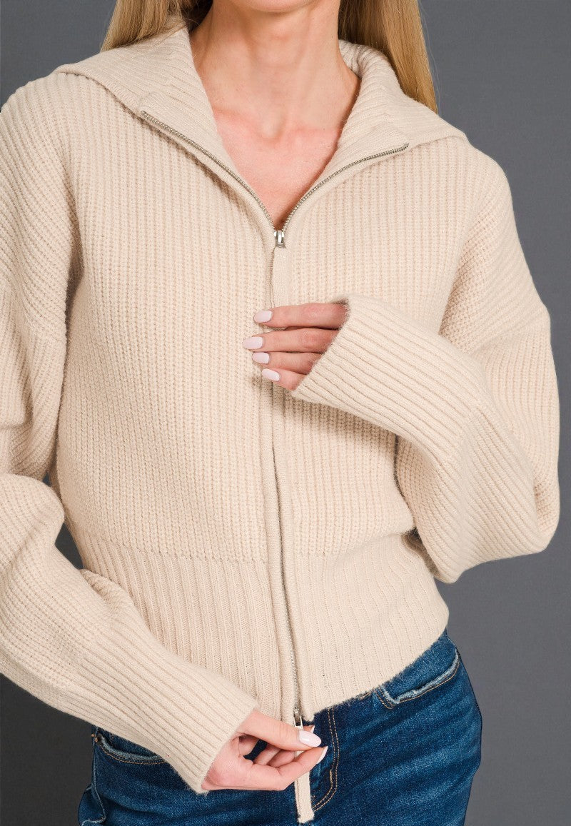 Beige zip-up sweater worn by a person on a gray background