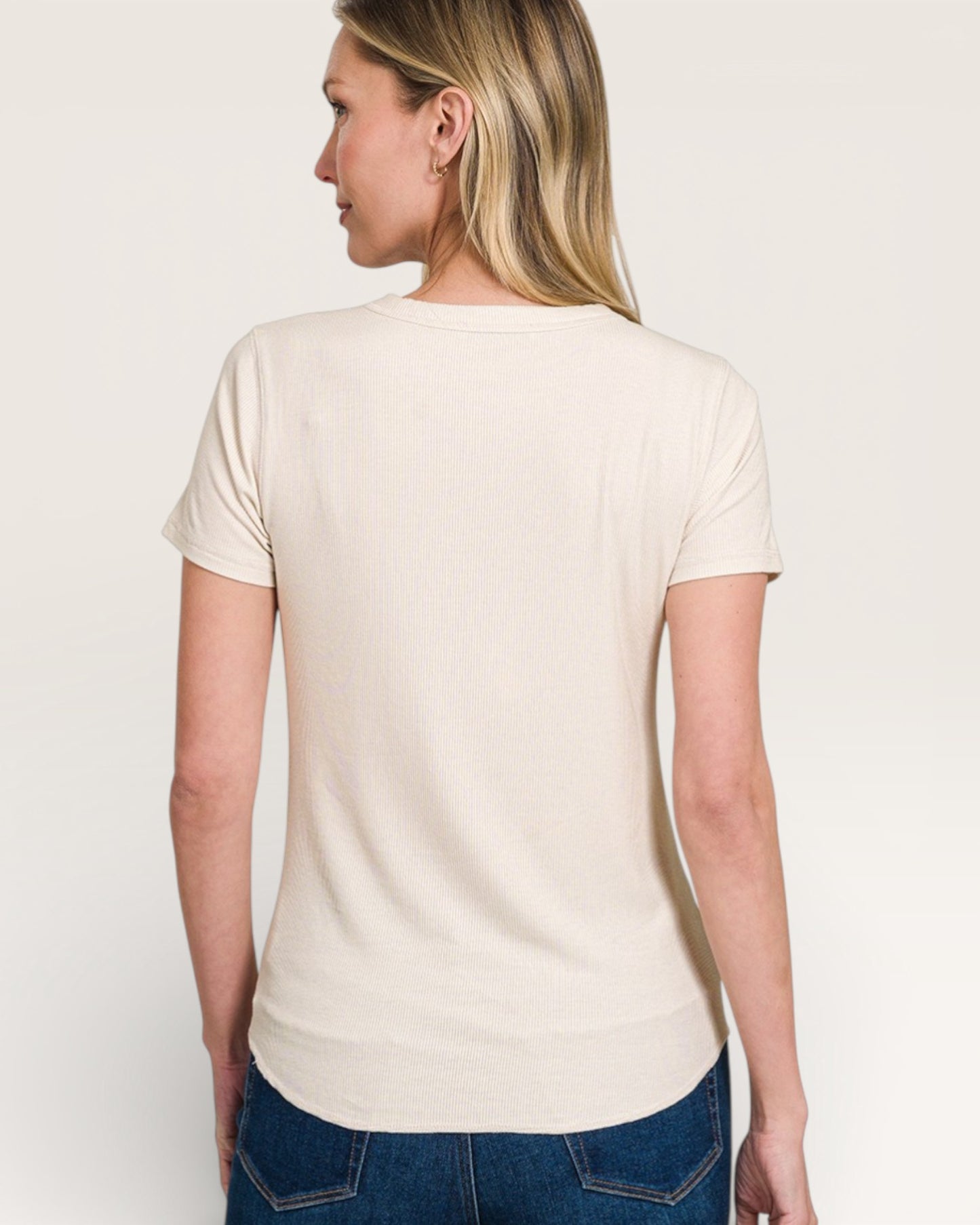 Woman wearing a beige t-shirt and blue jeans against a white background