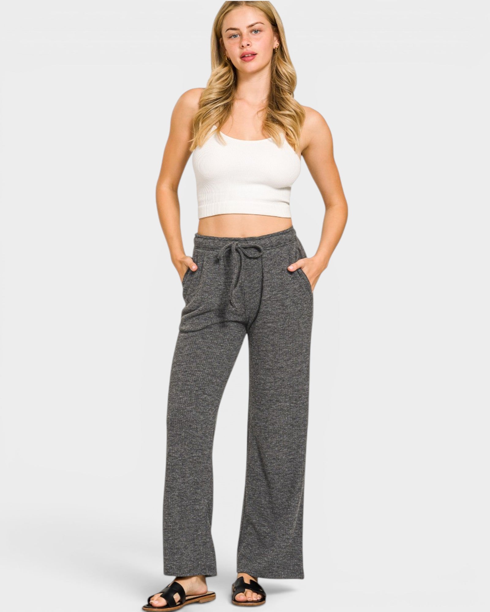Woman wearing gray drawstring pants and a white top on a white background