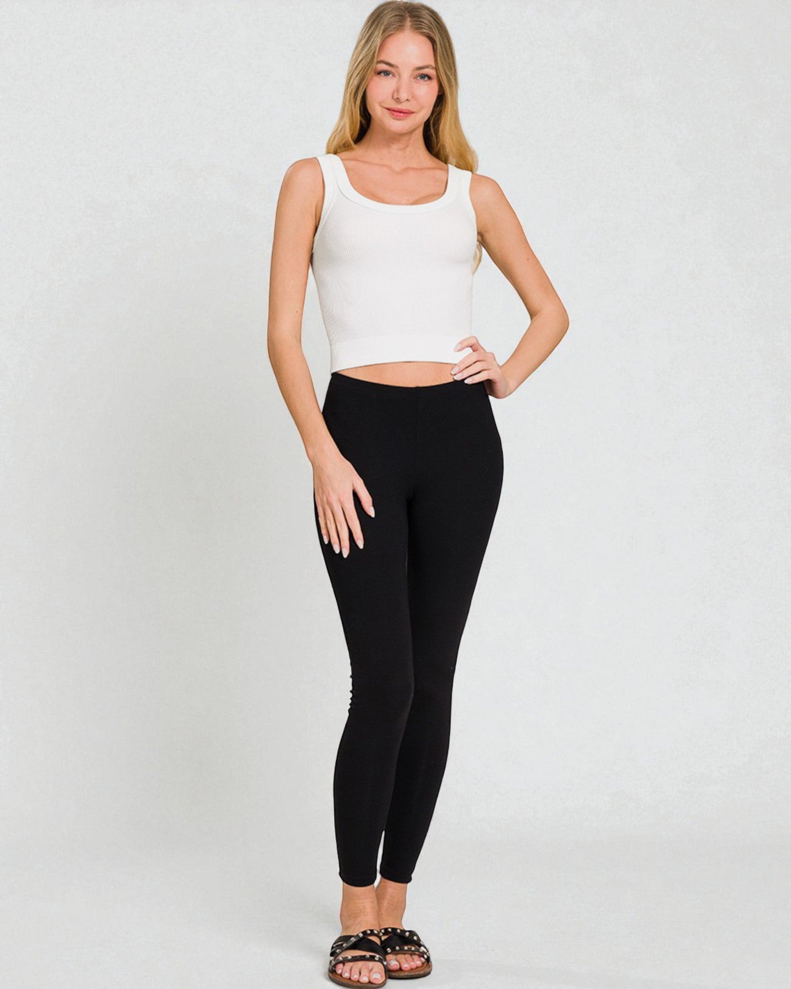 Woman wearing a white sleeveless top and black leggings on a plain background