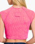 A close-up back view of a woman wearing a bright pink ribbed crop top with raglan sleeves and a small square patch detail on the upper back.