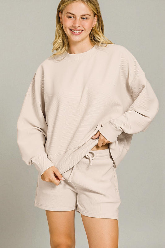 Woman wearing a beige sweatshirt and shorts set against a plain background