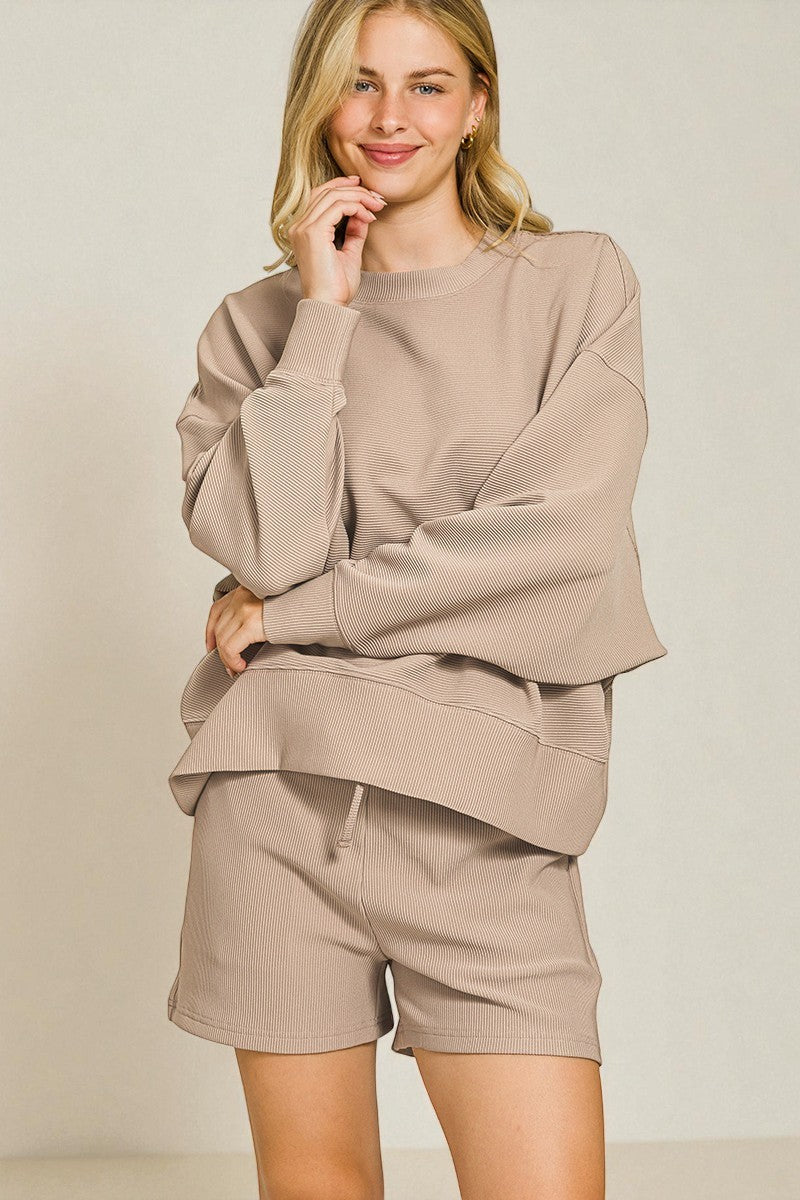 Woman wearing a beige sweatshirt and shorts set against a plain background