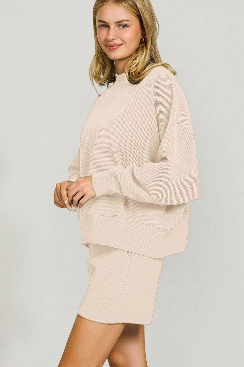 Woman wearing a beige sweater and skirt set against a plain background