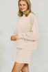 Woman wearing a beige sweater and skirt set against a plain background