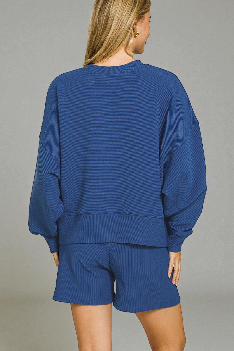 Person wearing a blue sweatshirt and shorts set against a gray background