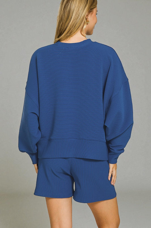 Person wearing a blue sweatshirt and shorts set against a gray background