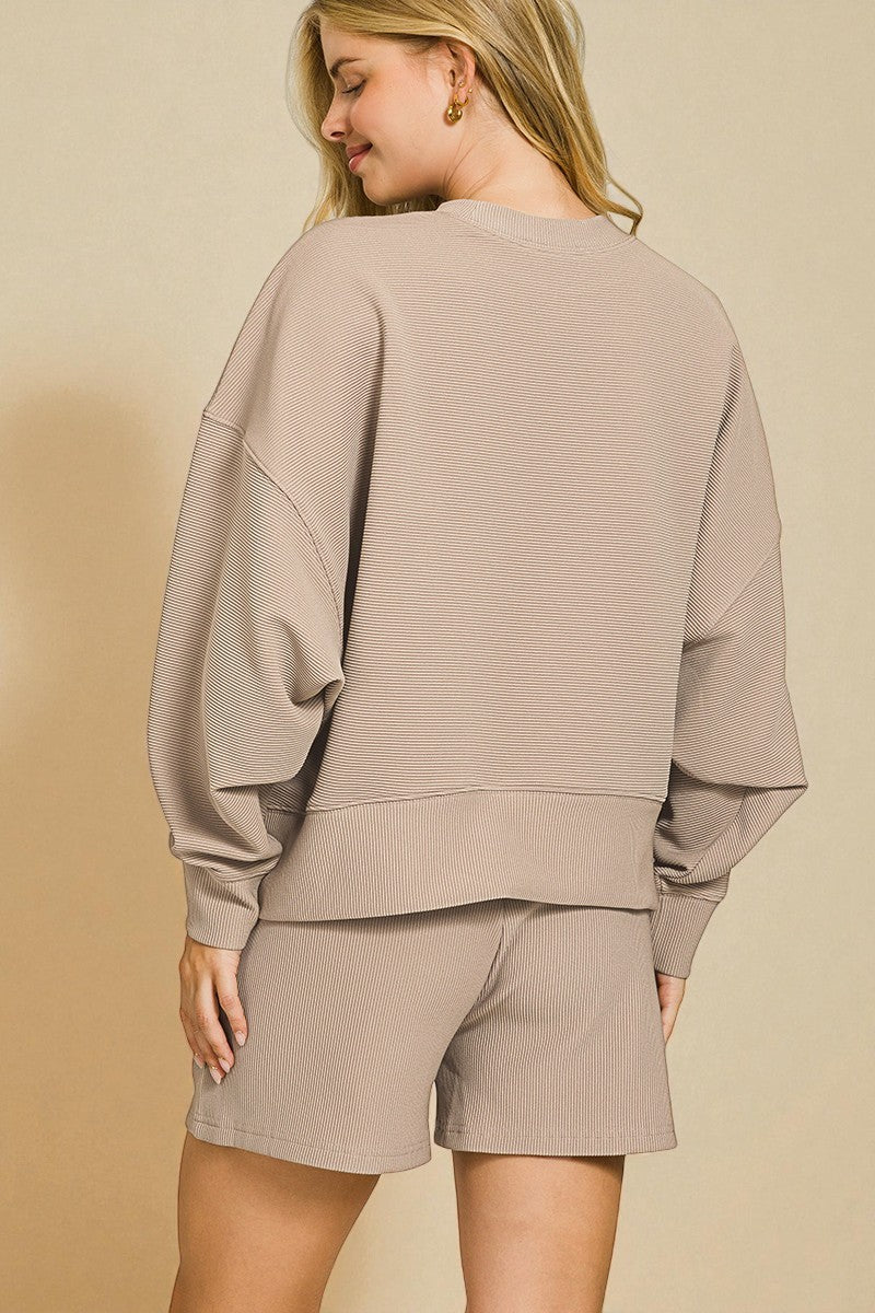 Woman wearing a beige sweatshirt and shorts set against a beige background