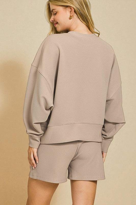 Woman wearing a beige sweatshirt and shorts set against a beige background