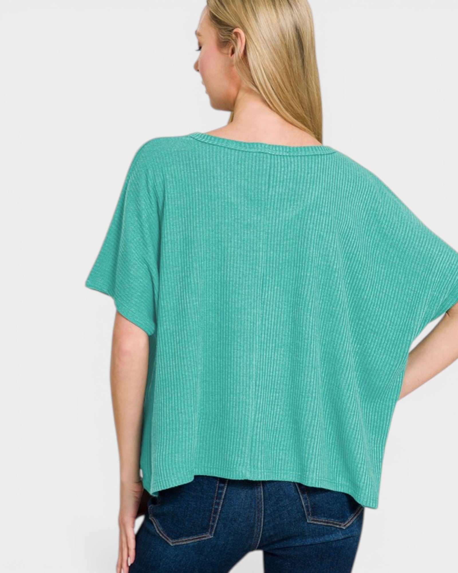 Woman wearing a teal ribbed top and blue jeans on a white background