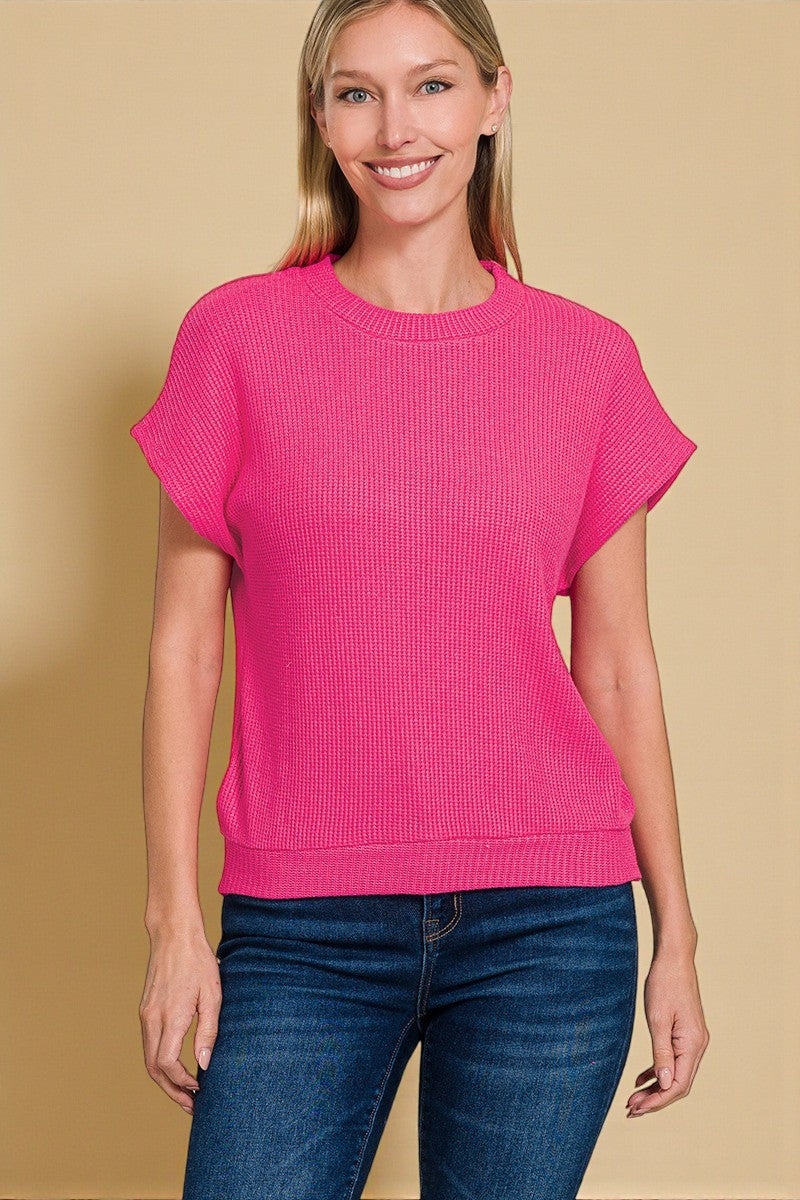 Woman wearing a bright pink sweater and blue jeans against a beige background