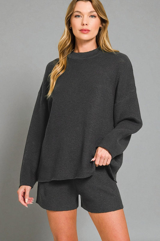 Woman wearing a dark gray sweater and shorts set against a gray background