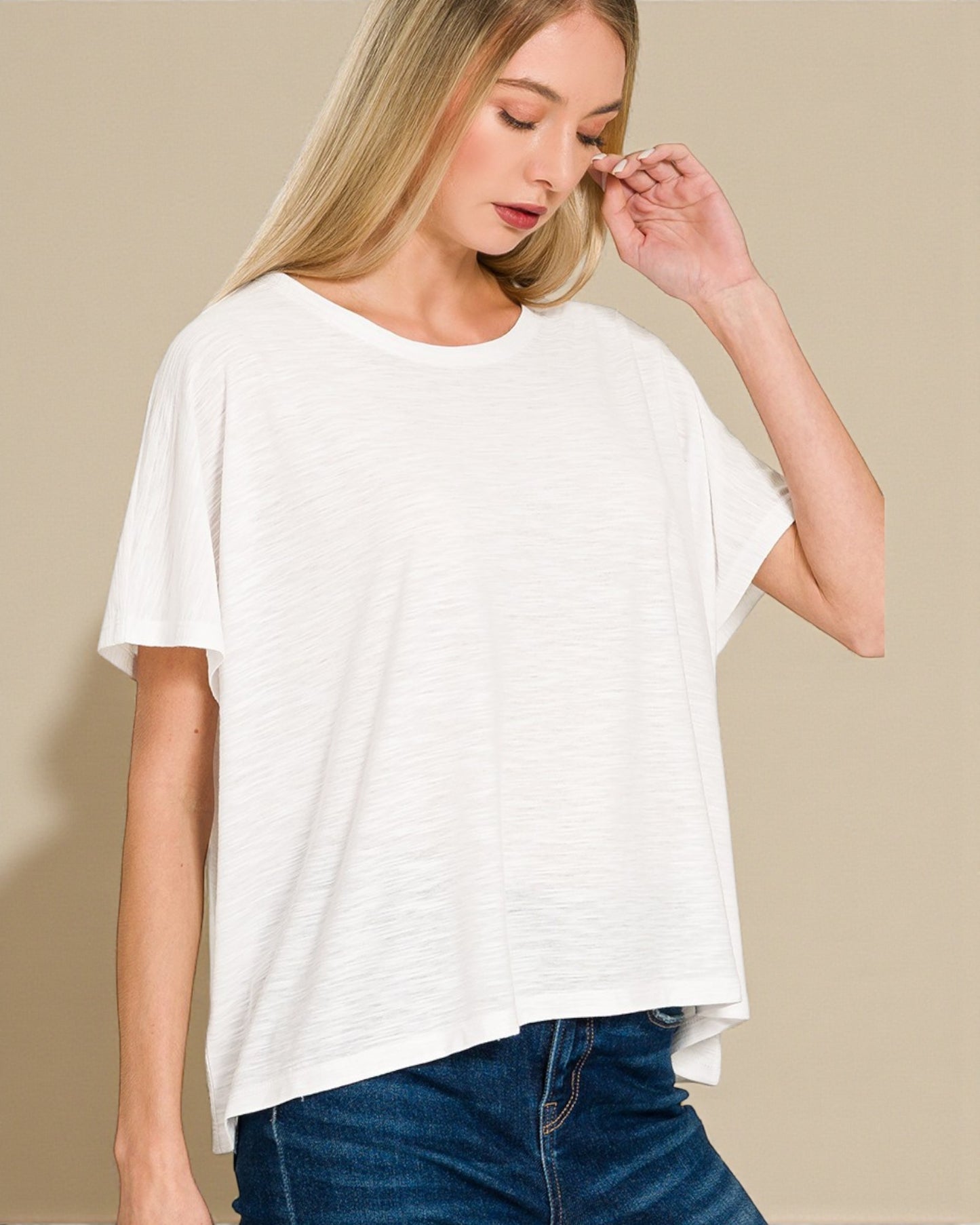 Woman wearing a white oversized t-shirt and blue jeans against a beige background