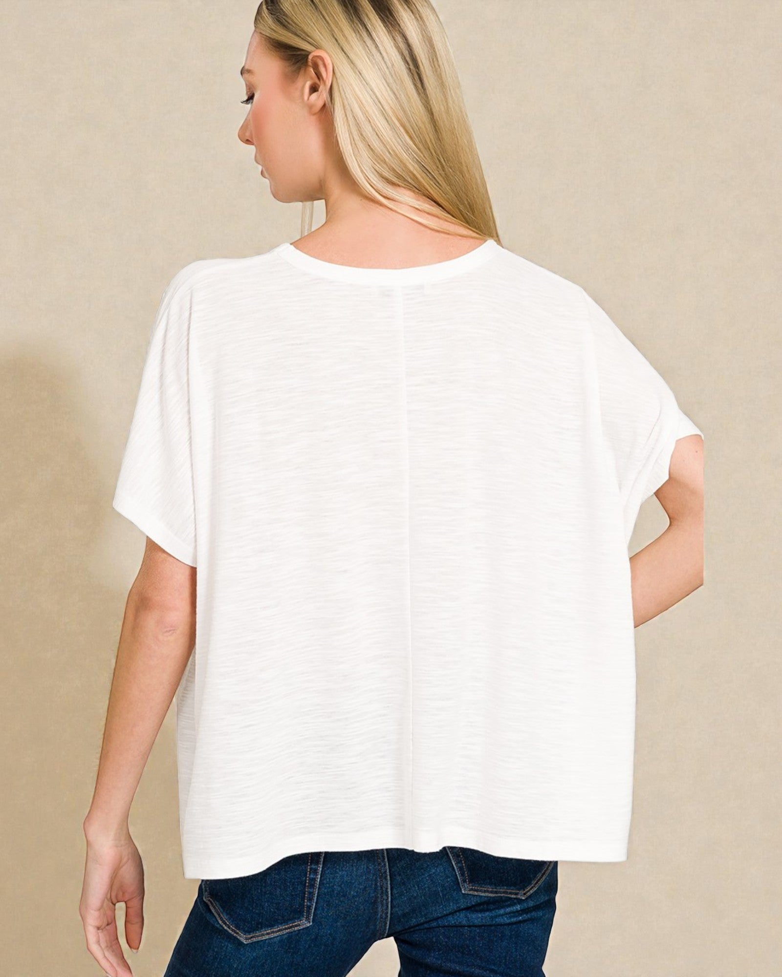 Woman wearing a white t-shirt and blue jeans against a beige background