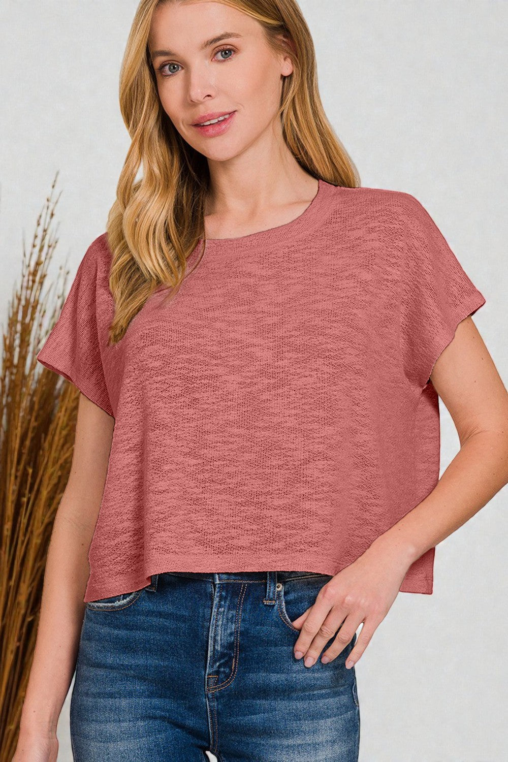 Woman wearing a pink top and blue jeans against a plain background